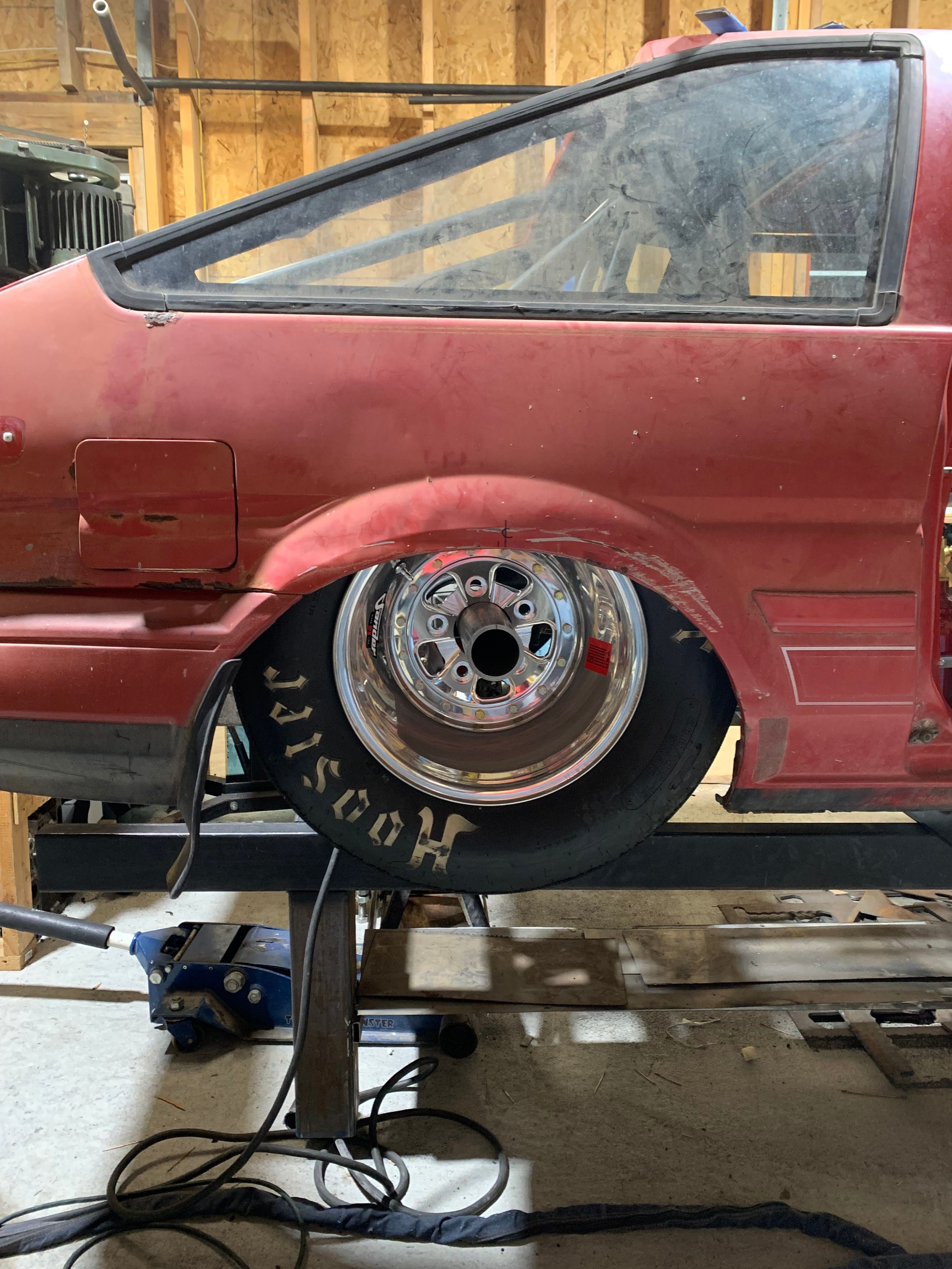 Red vehicle with a large wheel, partially visible, on a workbench in a workshop.