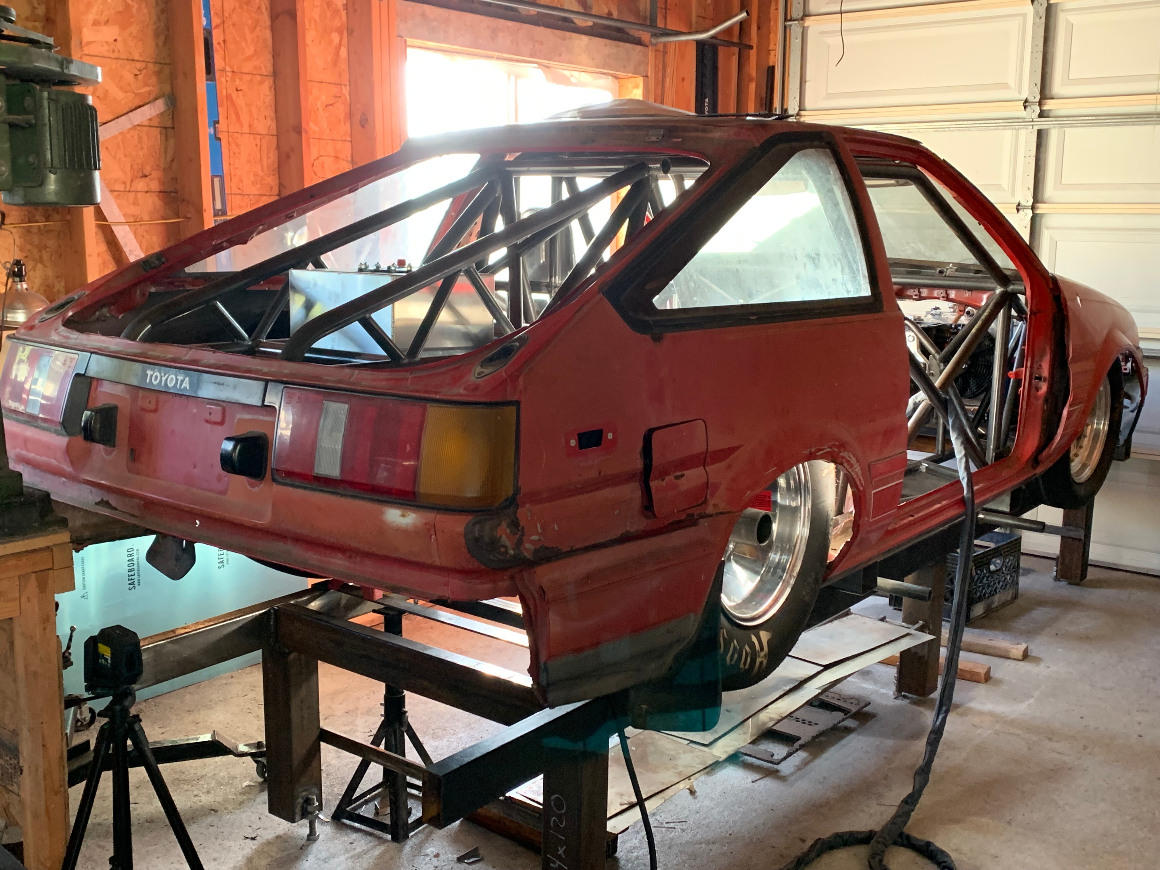 Red vintage car with missing front and rear panels, inside a garage, elevated on a platform, with visible interior and wheels.