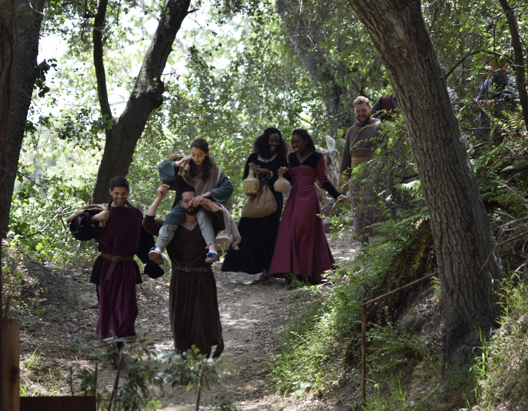 Group of people walking on a forest trail surrounded by trees and greenery.