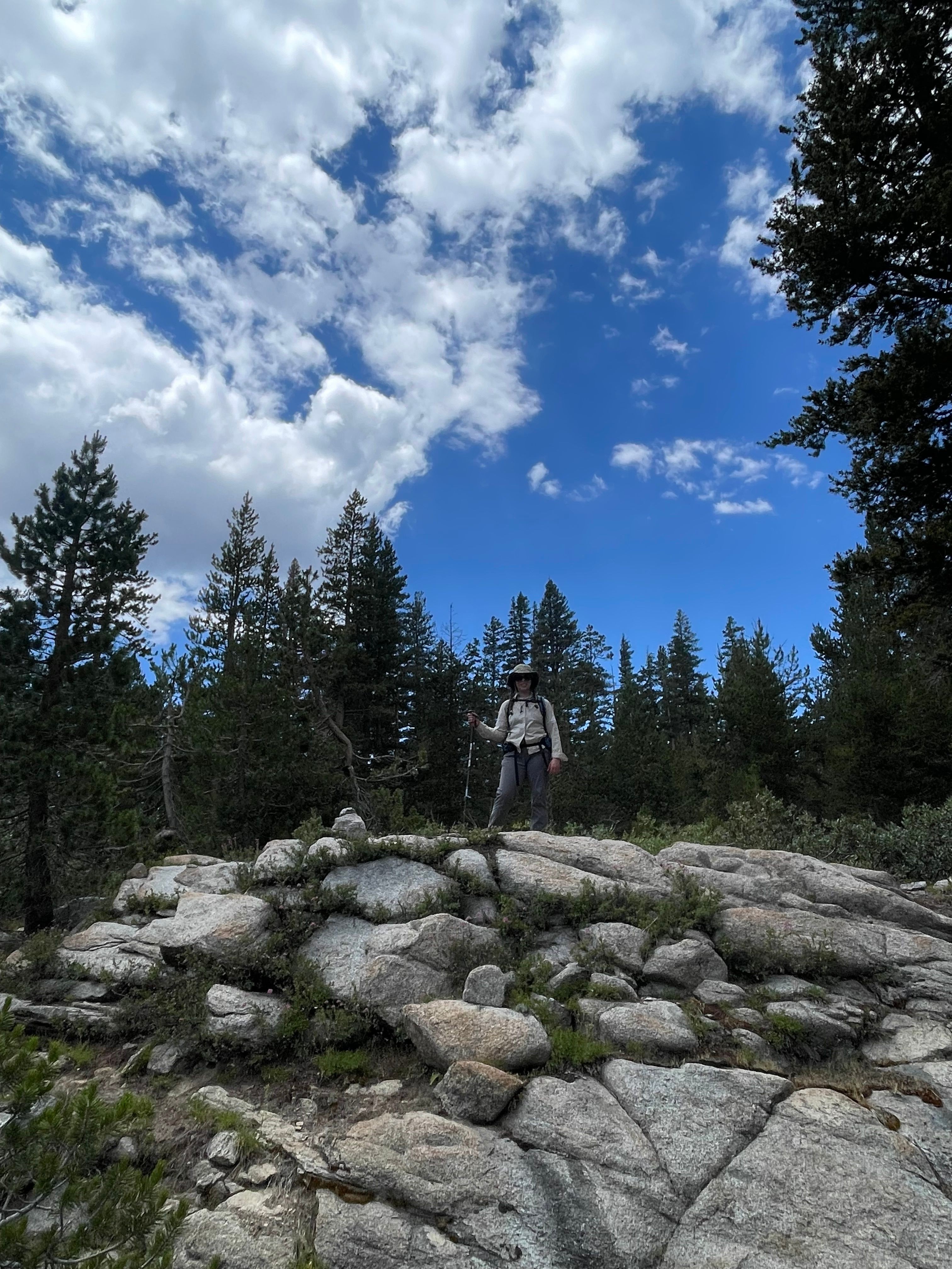 Rocky terrain with trees and a person in the distance under a partly cloudy sky.