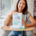 Smiling woman sitting at a table with a book titled 'The Rewire Retirement Method' in front of her.