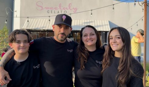 Four people standing outdoors in front of a building with a sign that reads "Sweetably Gelato." They are smiling and wearing black shirts.