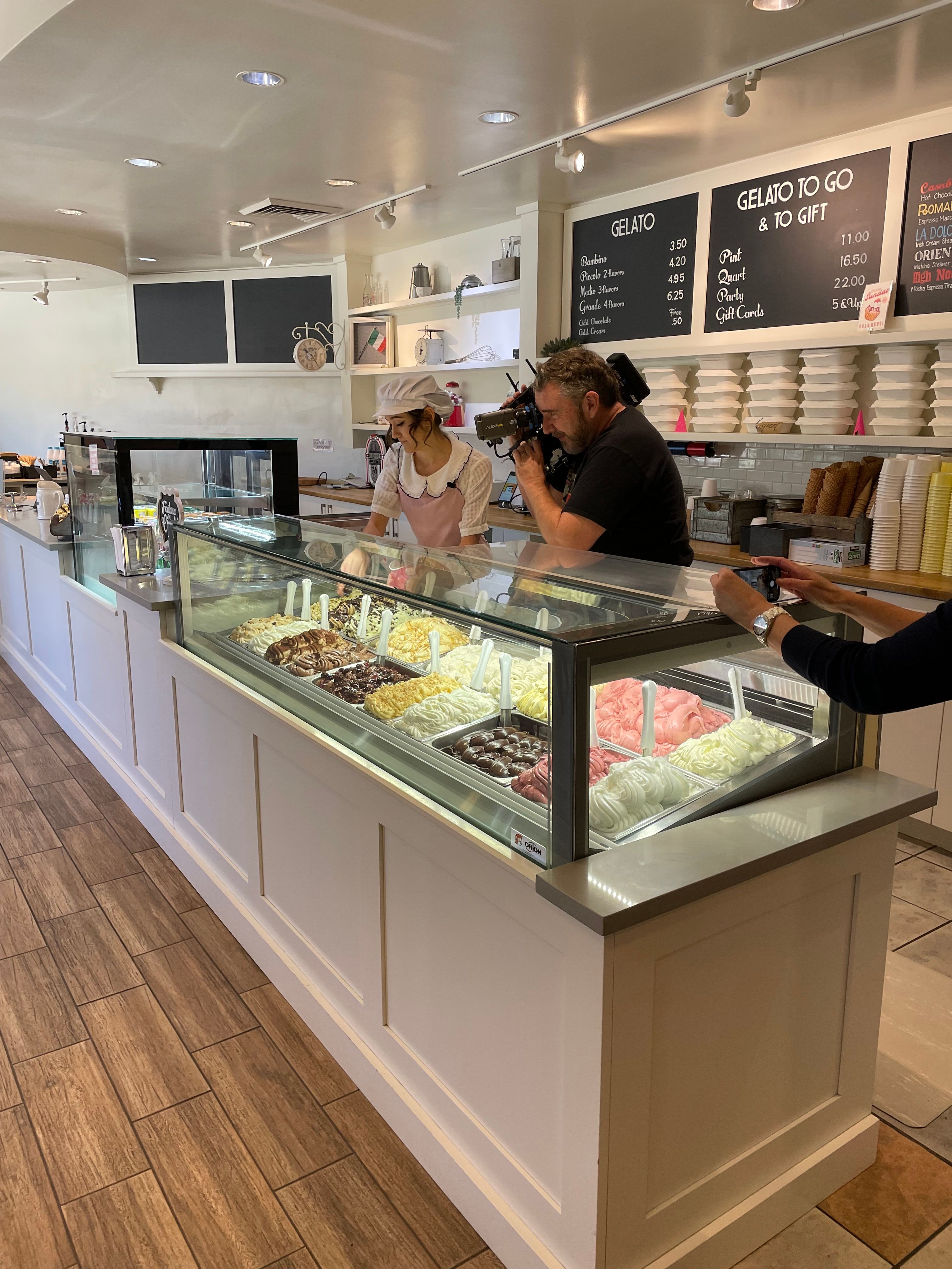 People shopping at a grocery store's ice cream display, with shelves and a digital screen in the background.
