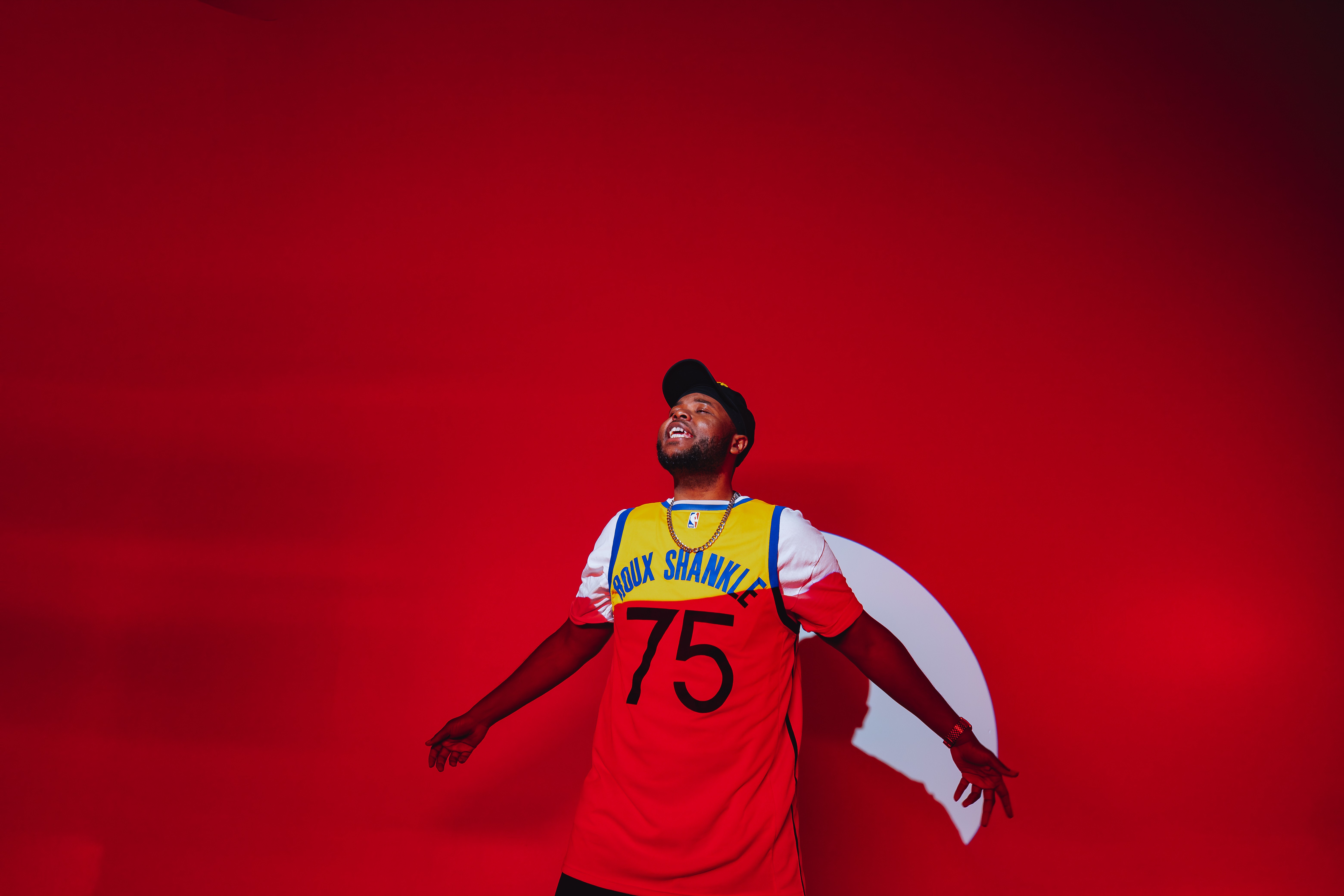 A person wearing a red sports jersey with the number 75, smiling with arms outstretched against a red background.