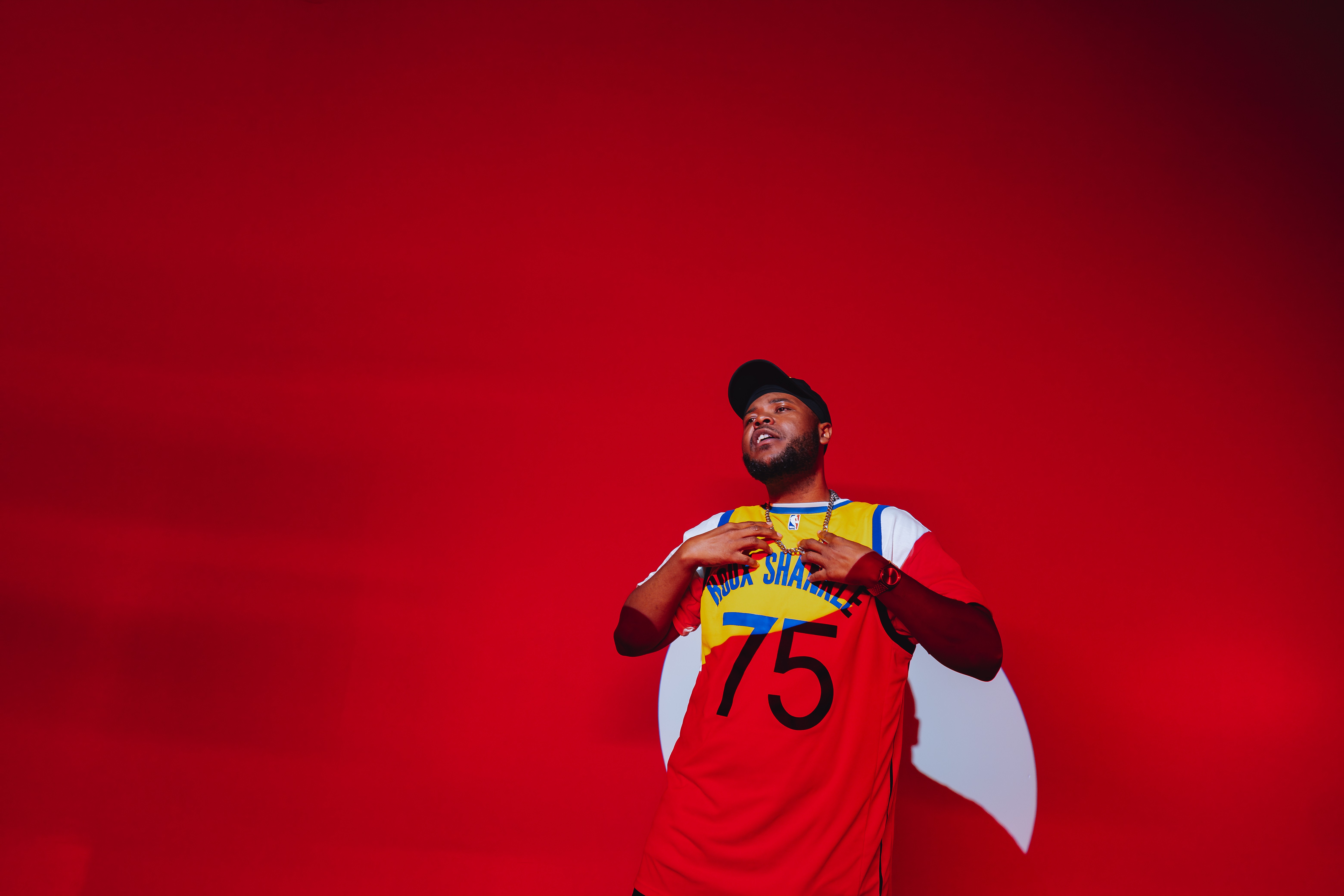 Person wearing a red sports jersey with the number 75, holding a medal, against a red background.
