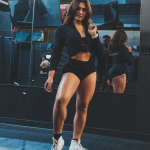 Woman in workout clothes taking a mirror selfie in a gym, with mirrors reflecting her back and surroundings.