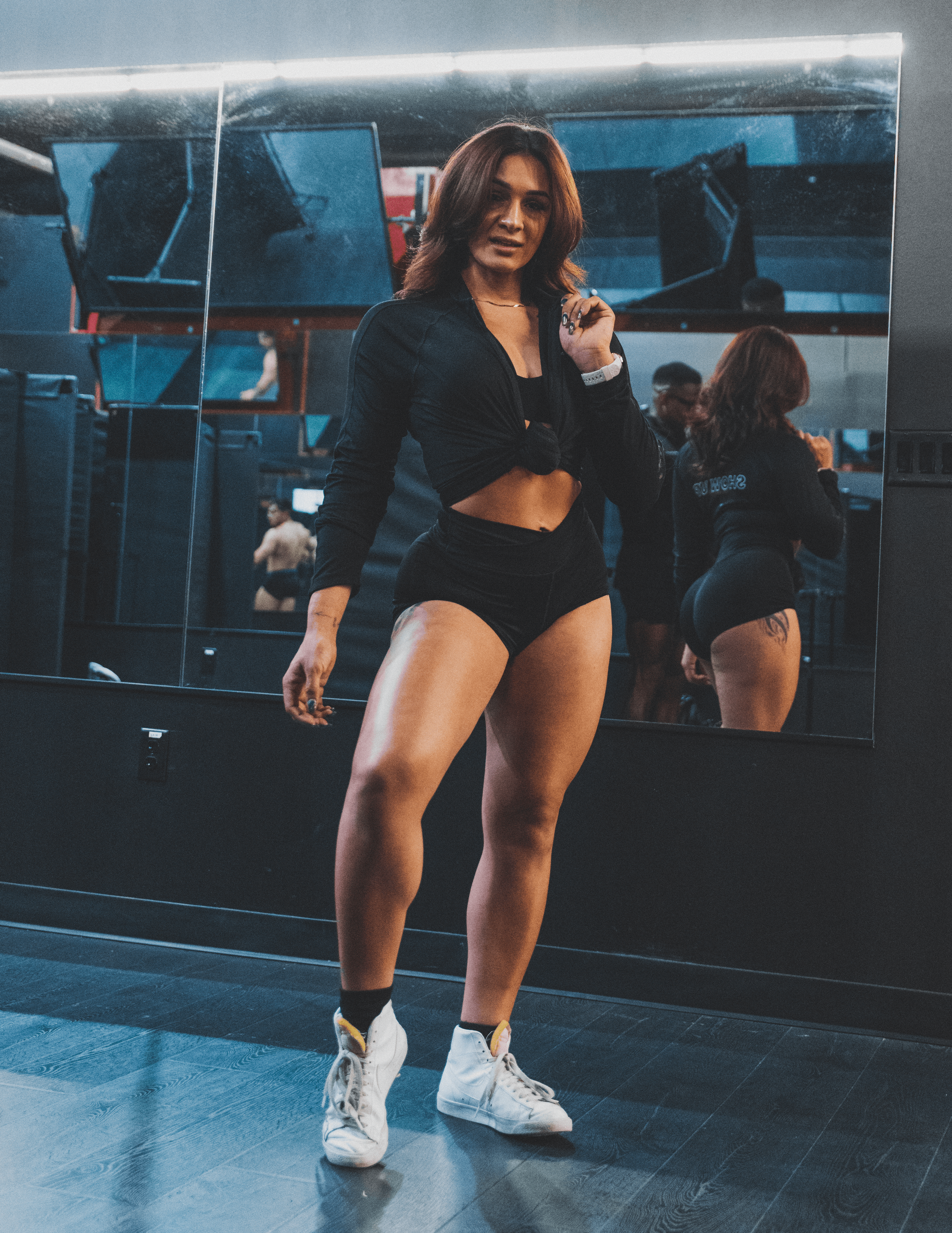Woman in workout clothes taking a mirror selfie in a gym, with mirrors reflecting her back and surroundings.