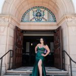 Woman in a green gown with a high slit standing in front of an ornate building entrance, hands on hips.