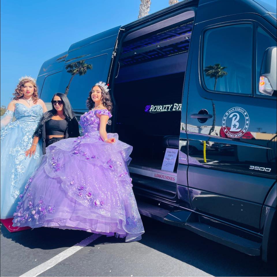 Three women in formal dresses standing outside a black vehicle with an open door, palm trees in the background.