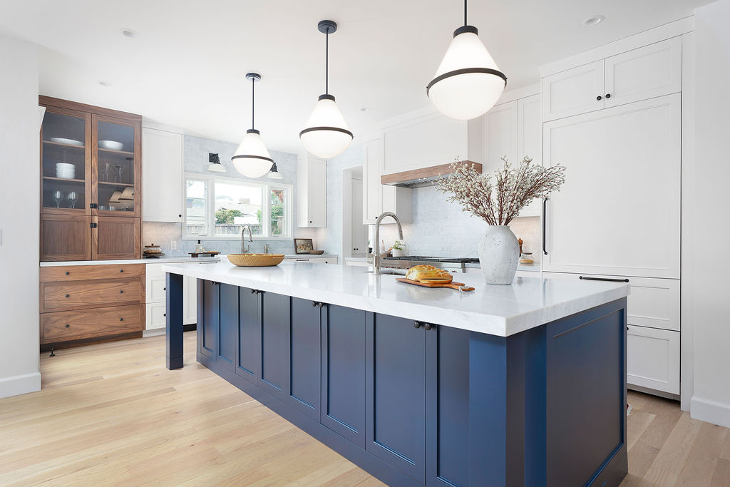 Modern kitchen with white cabinets, a blue island, pendant lights, and a wooden cabinet, with a vase and plants on the island.