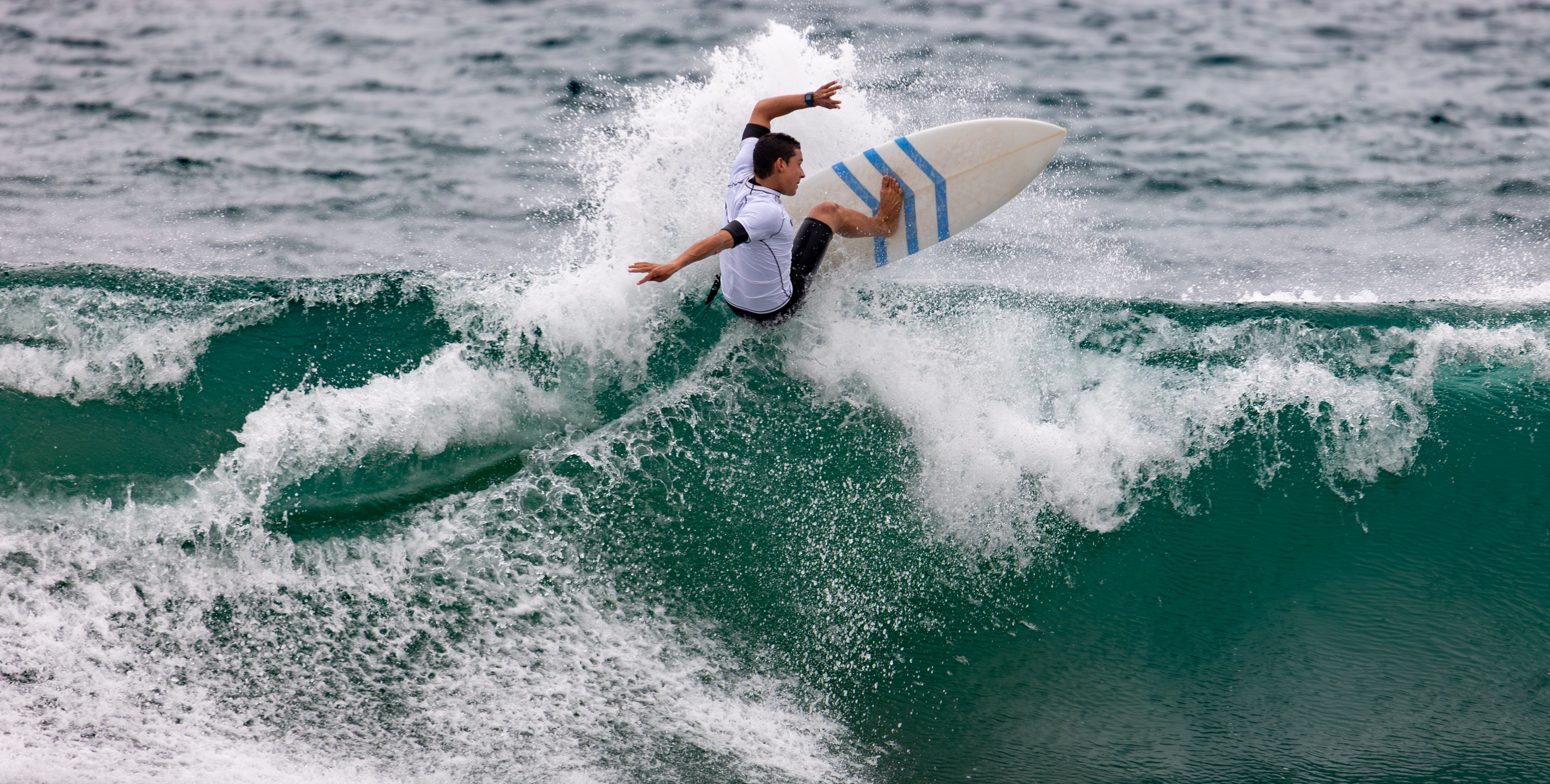 Person surfing on a wave, wearing a white shirt and dark shorts, with water splashing around.