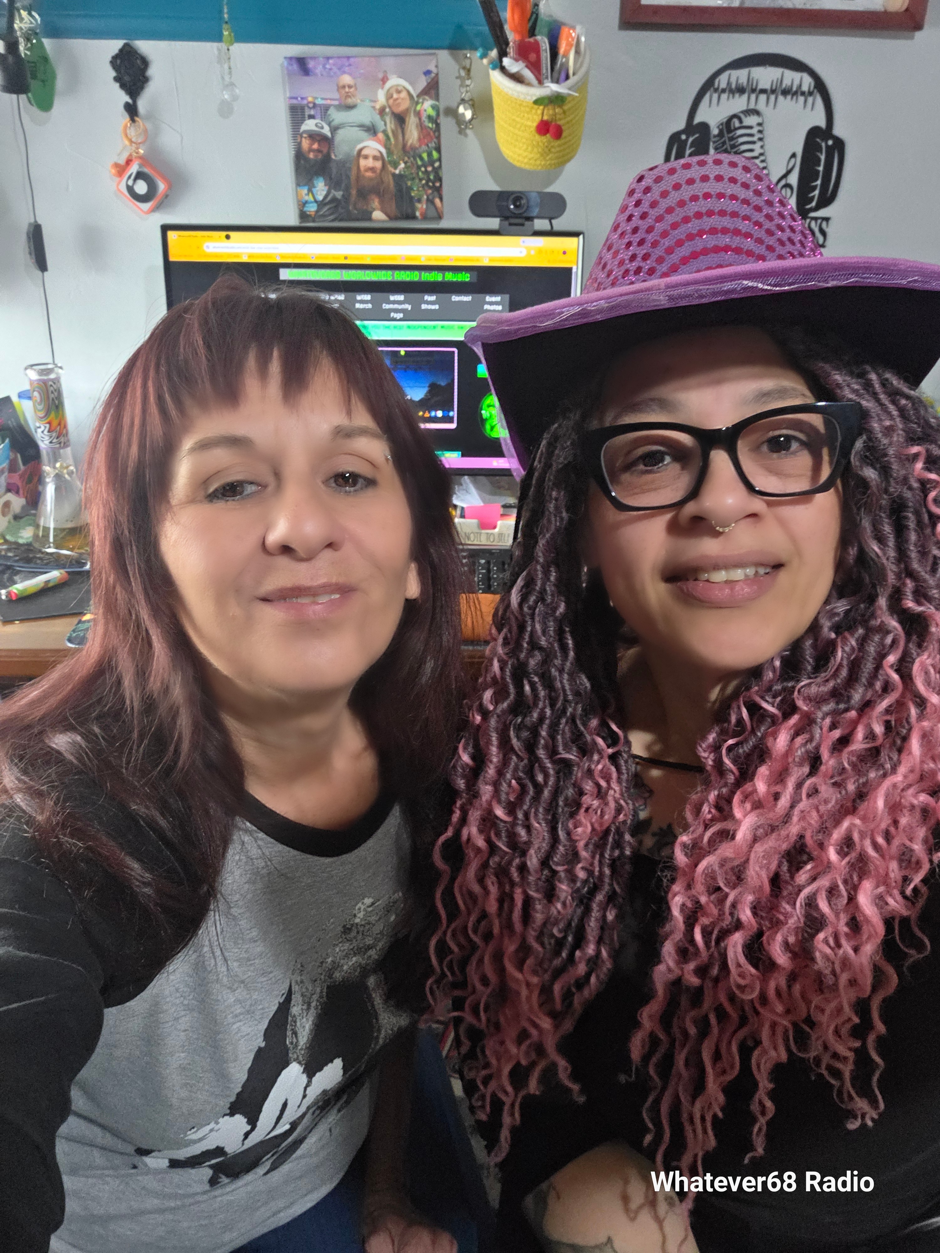 Two women smiling in front of a computer with colorful decorations in the background.