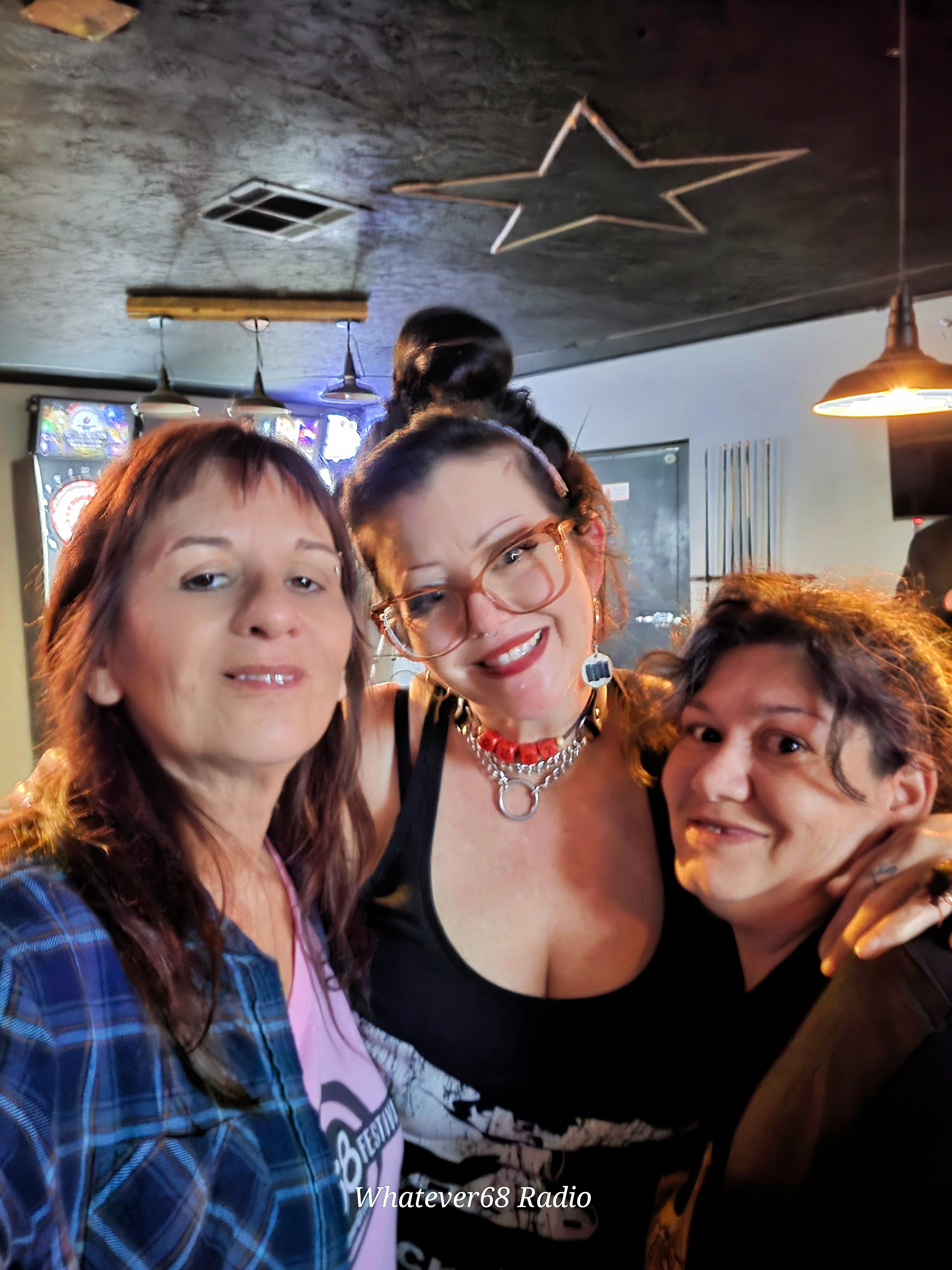 Three women smiling together indoors with star-shaped ceiling decoration and hanging lights, posing for a photo.