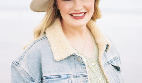 Smiling woman wearing a wide-brimmed hat and denim jacket outdoors, light background.